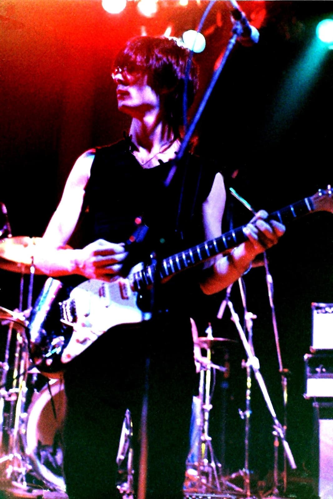 Lenny Kaye, dark-haired, playing an electric guitar under red and blue stage light