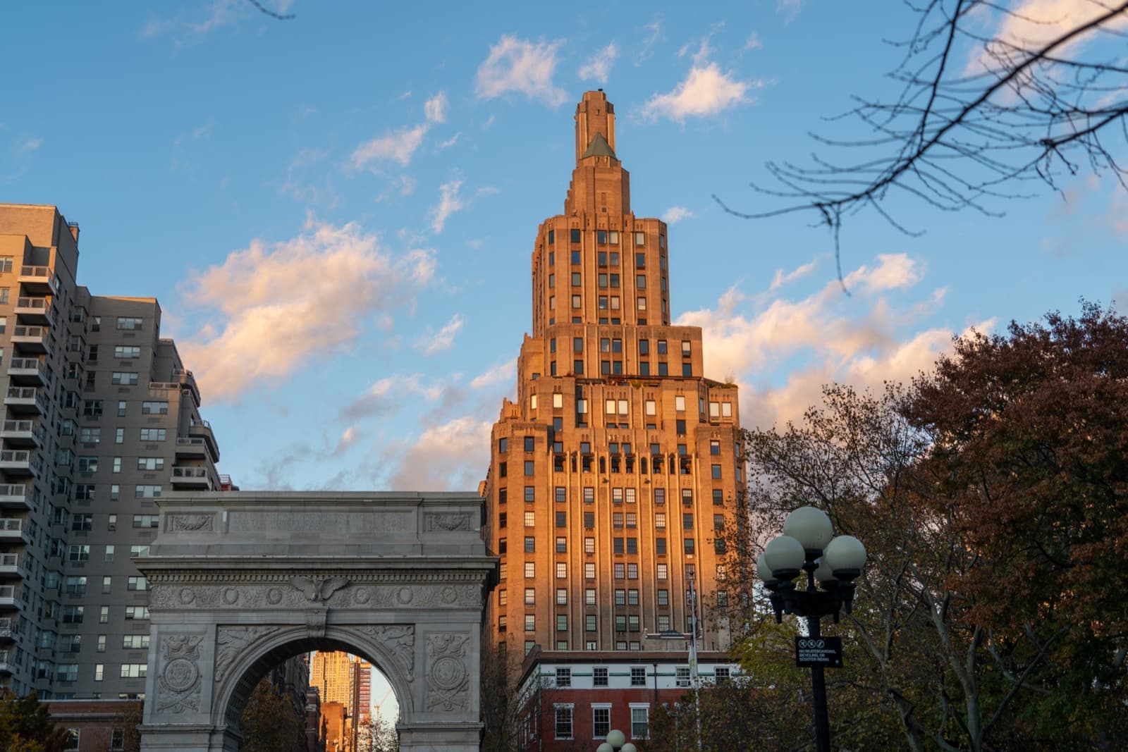 A stepped Art Deco tower lit gold by low sun, with the Washington Square Arch in front