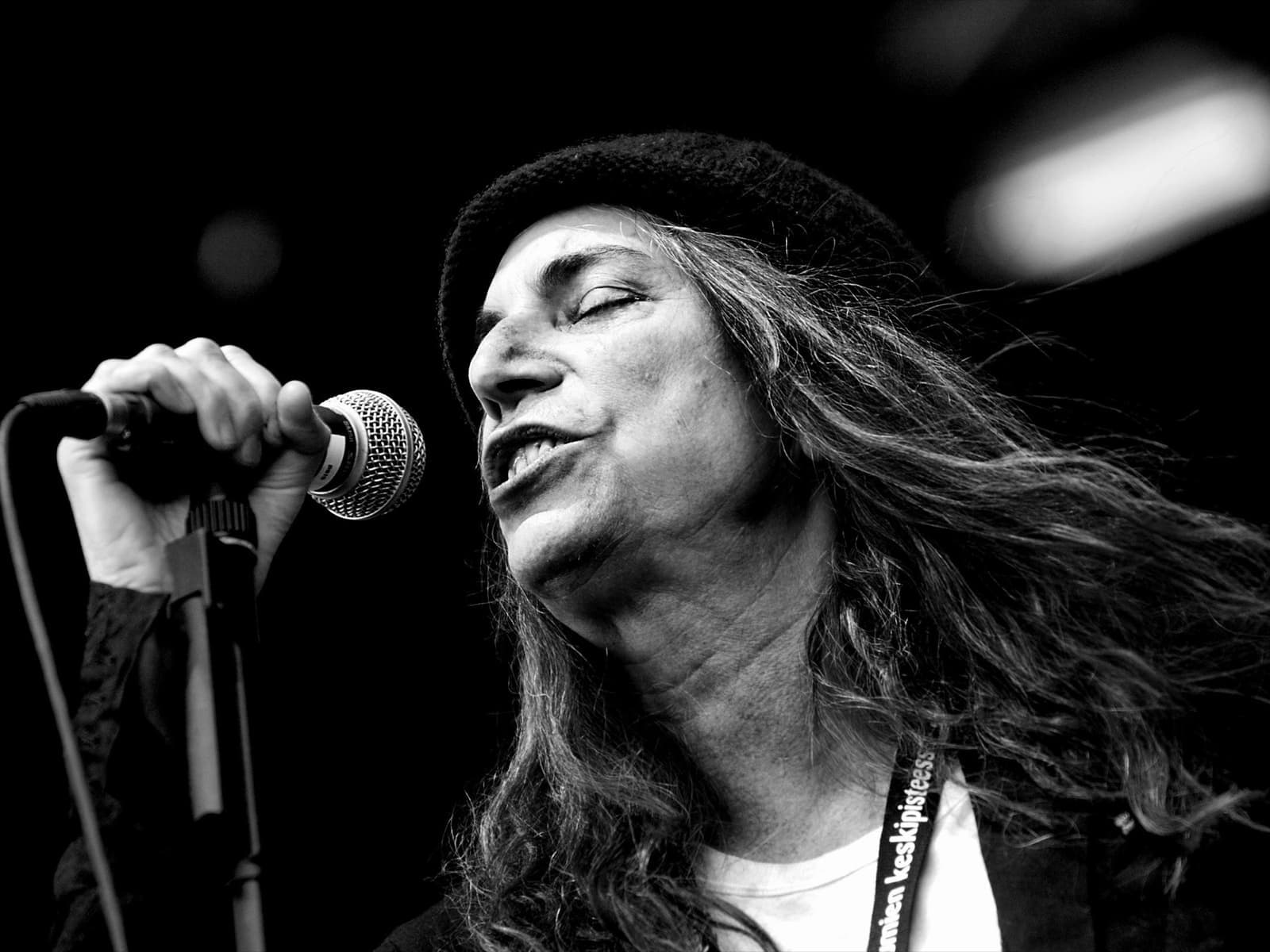 Patti Smith in a black knit cap singing into a microphone, eyes closed, in black and white