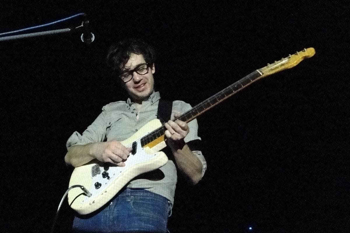 Laurent Brancowitz in glasses playing a white guitar