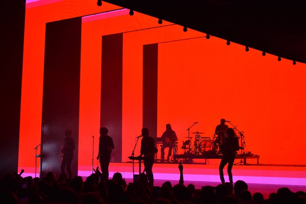 The band in silhouette against a red stage backdrop with tall black panels