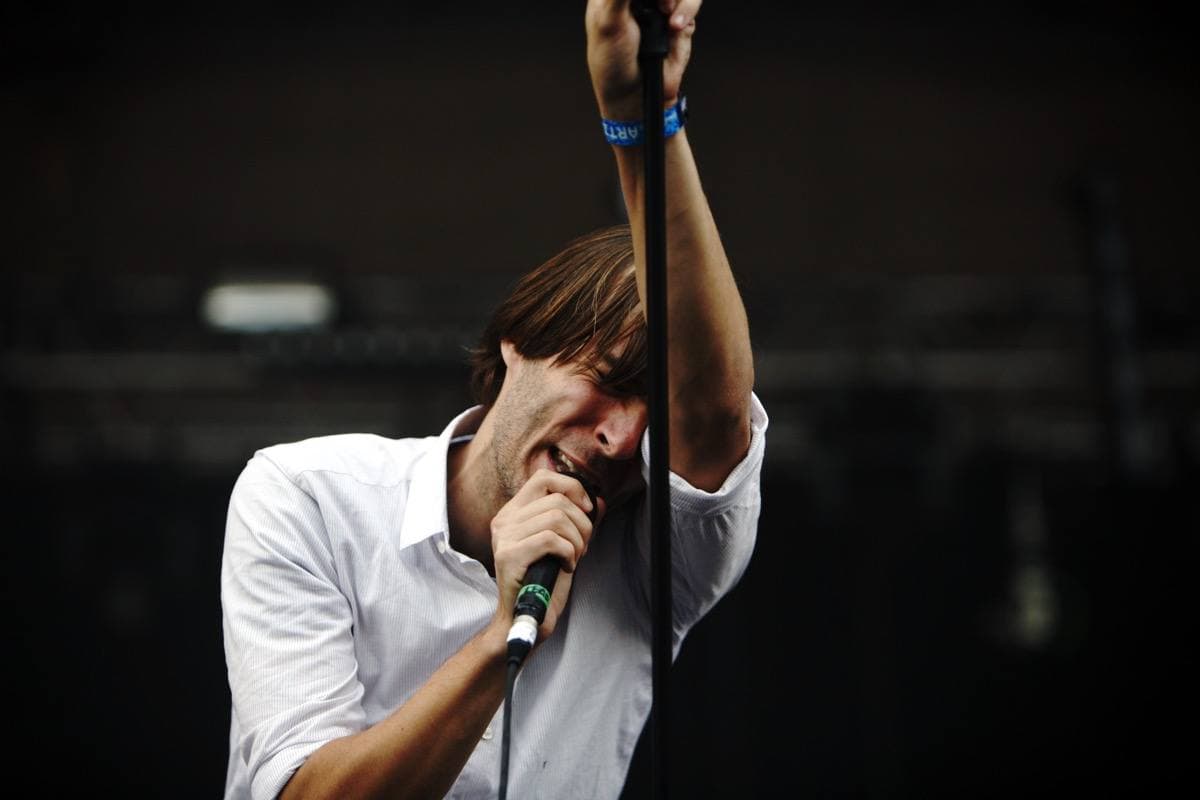 Thomas Mars in a white shirt holding the microphone stand above his head, eyes closed