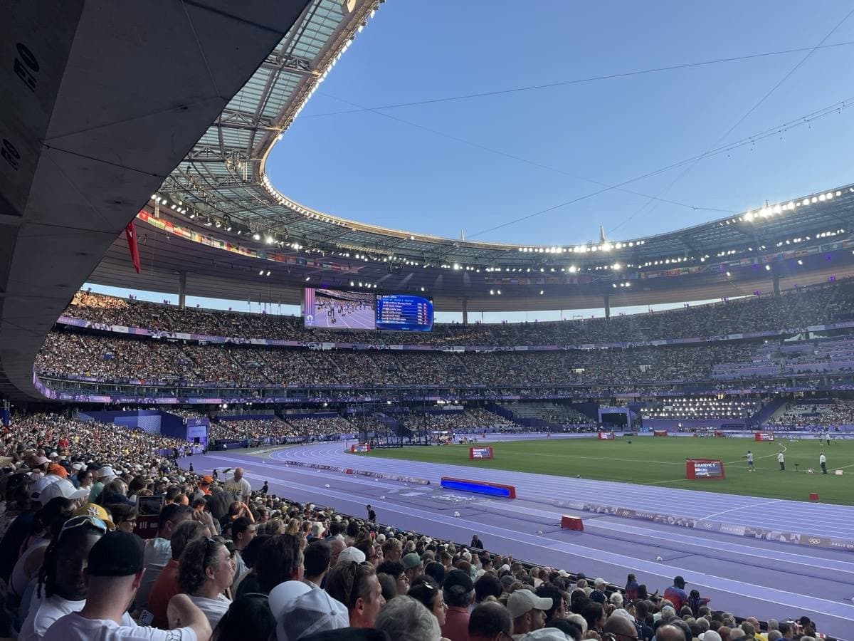 A packed stadium bowl with a purple running track under a blue evening sky