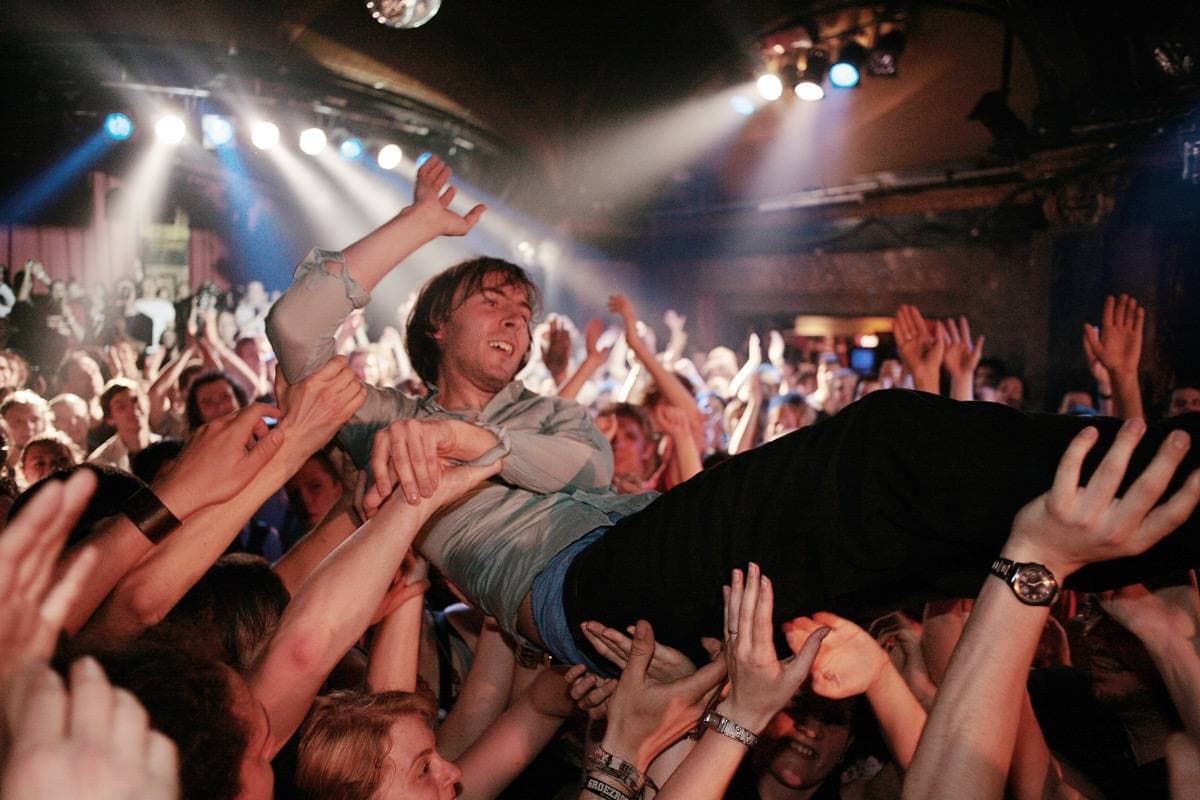 Thomas Mars lying across raised hands above a crowd, stage lights behind
