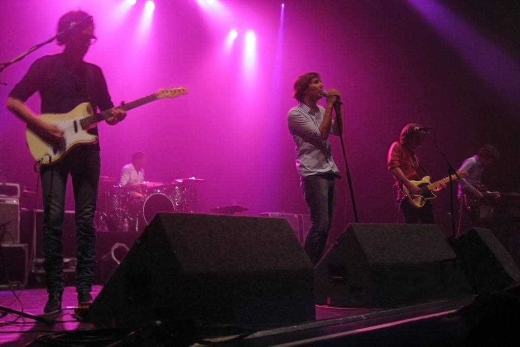The band on a stage washed in magenta light, guitars and drums