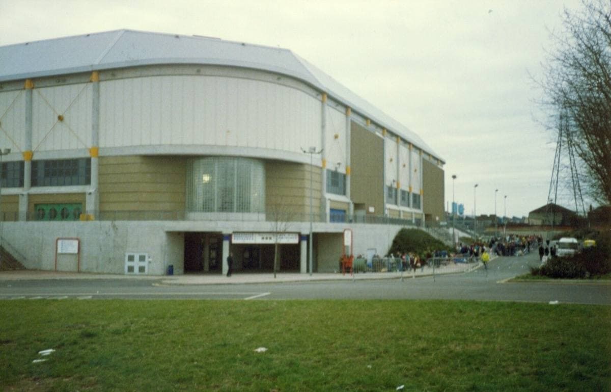 Sheffield Arena in 1993: a wide pale building with a curved roof beyond a strip of grass, people queueing along the front