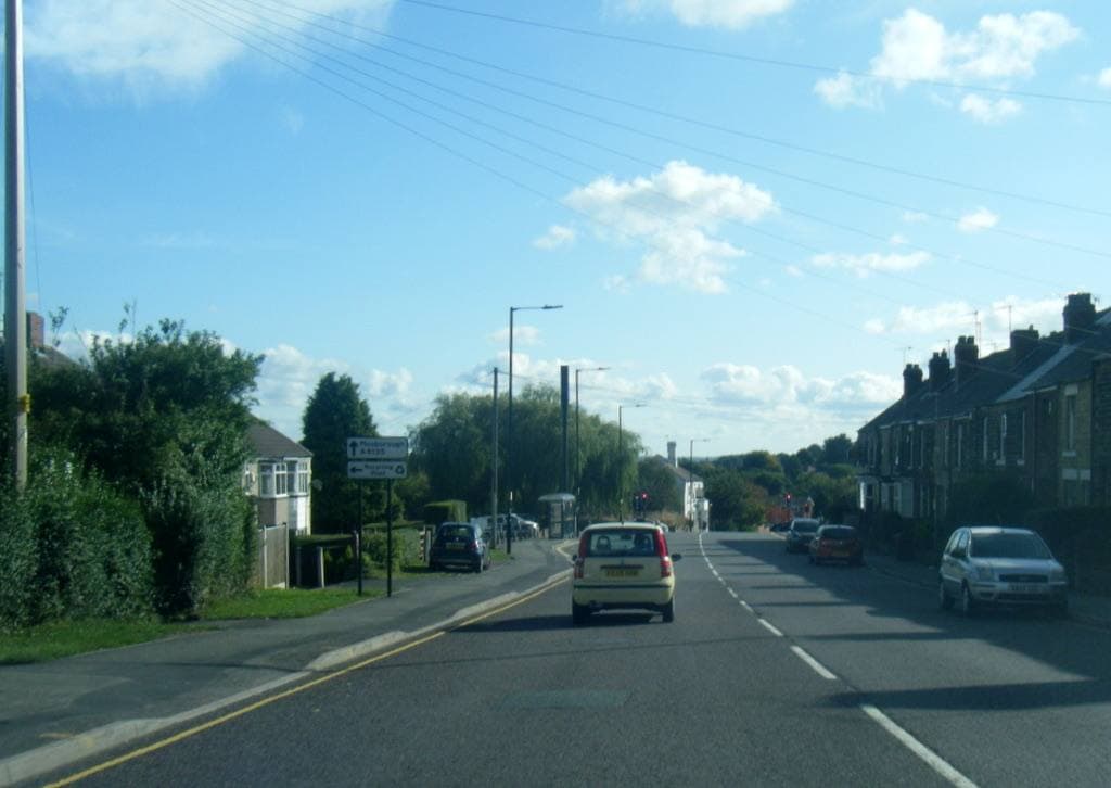 Mansfield Road in Intake, Sheffield: a long main road with cars, terraced houses and trees under a blue sky with white clouds
