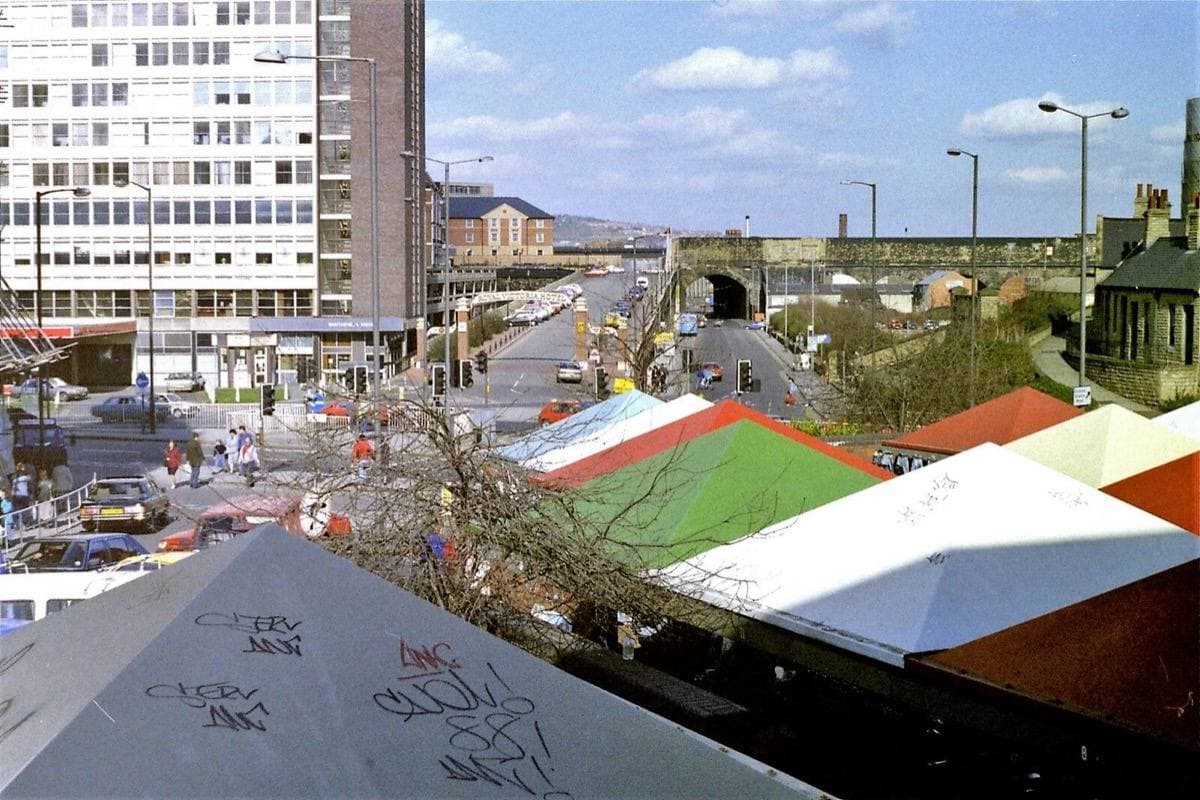 Looking out from Castle Market, Sheffield, in March 1989: red and green market stall roofs below, office blocks and roads beyond