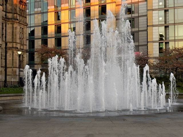 Fountain jets in the Peace Gardens, Sheffield, white water rising in front of a glass and stone building
