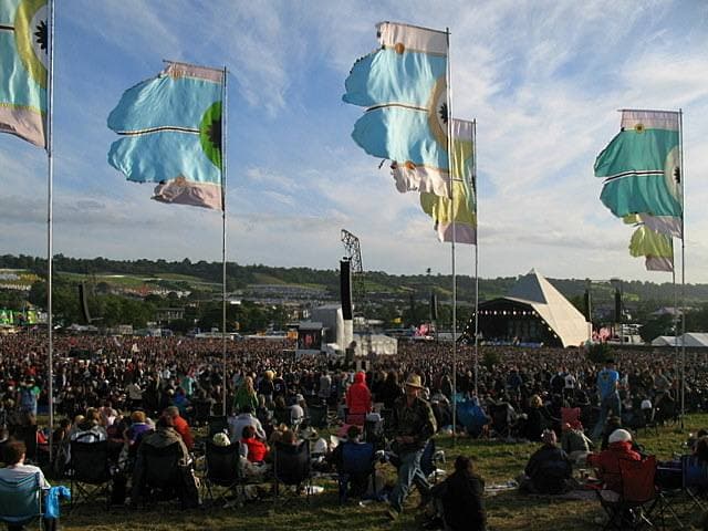 The Pyramid Stage at Glastonbury in 2008, early evening, flags blowing over a huge seated crowd