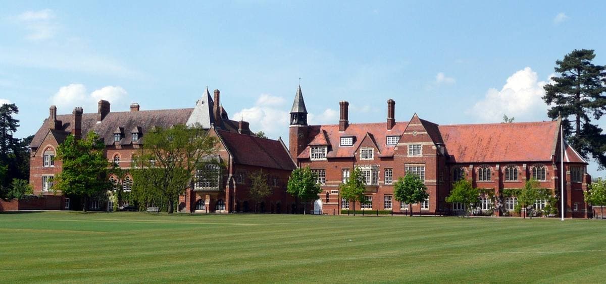 Red-brick Victorian school buildings with gables beyond a wide green field