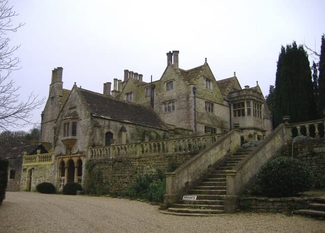 A grey stone Tudor manor with tall chimneys and a stone stair