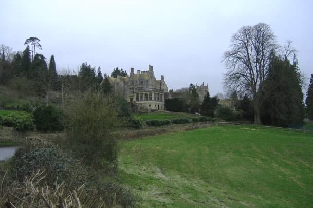 A stone manor among trees beyond a sloping green field