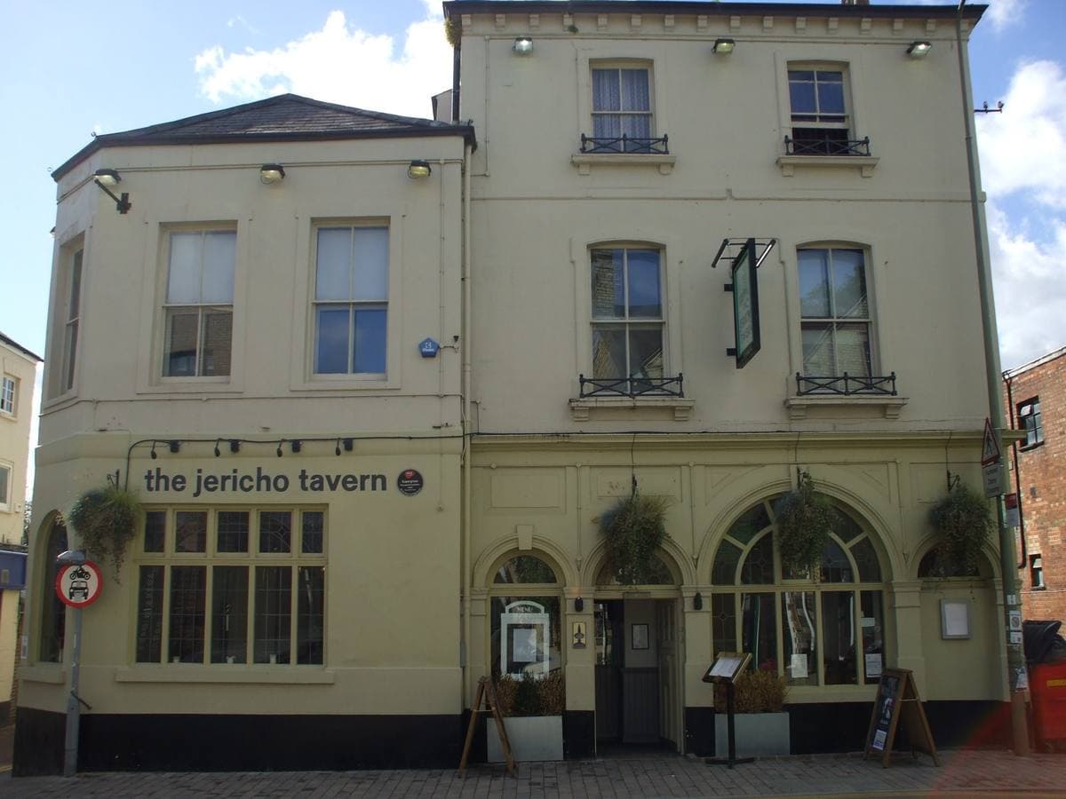 A cream-painted corner pub with tall windows and hanging baskets