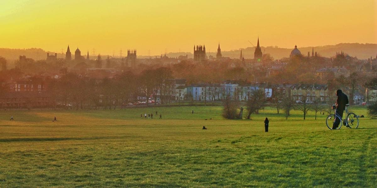 A wide grassy slope at sunset with the towers and spires of Oxford on the skyline
