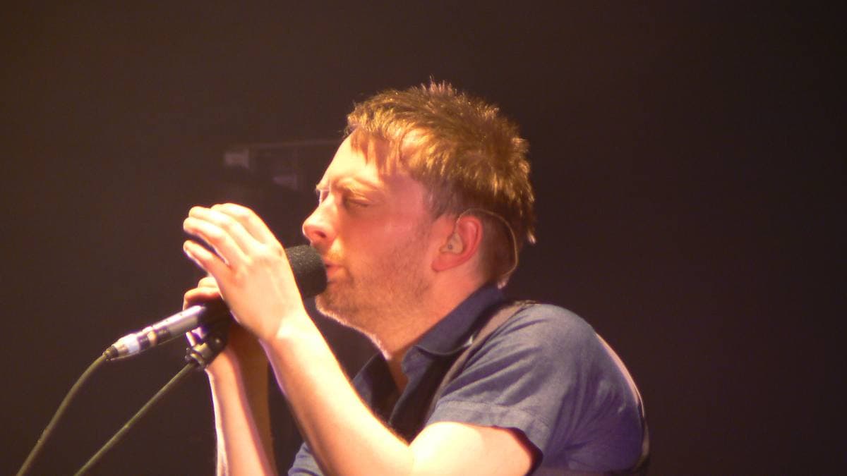 Thom Yorke singing into a hand-held microphone, lit amber