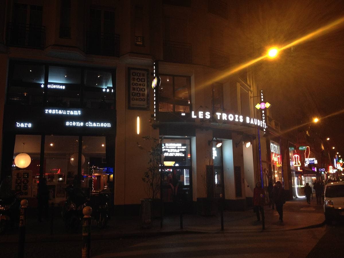 A lit venue front at night with LES TROIS BAUDETS above the door