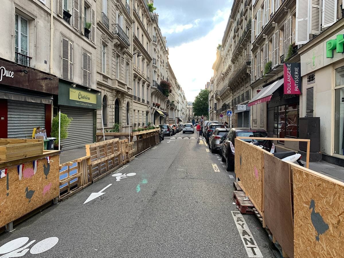 A street of Paris apartment buildings with shopfronts and parked cars
