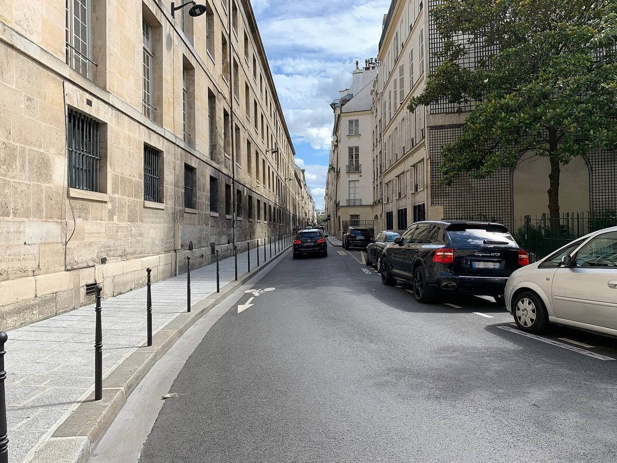 A narrow street of tall stone buildings with parked cars