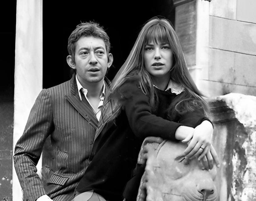 Serge Gainsbourg in a pinstriped jacket beside Jane Birkin, who leans on a stone lion