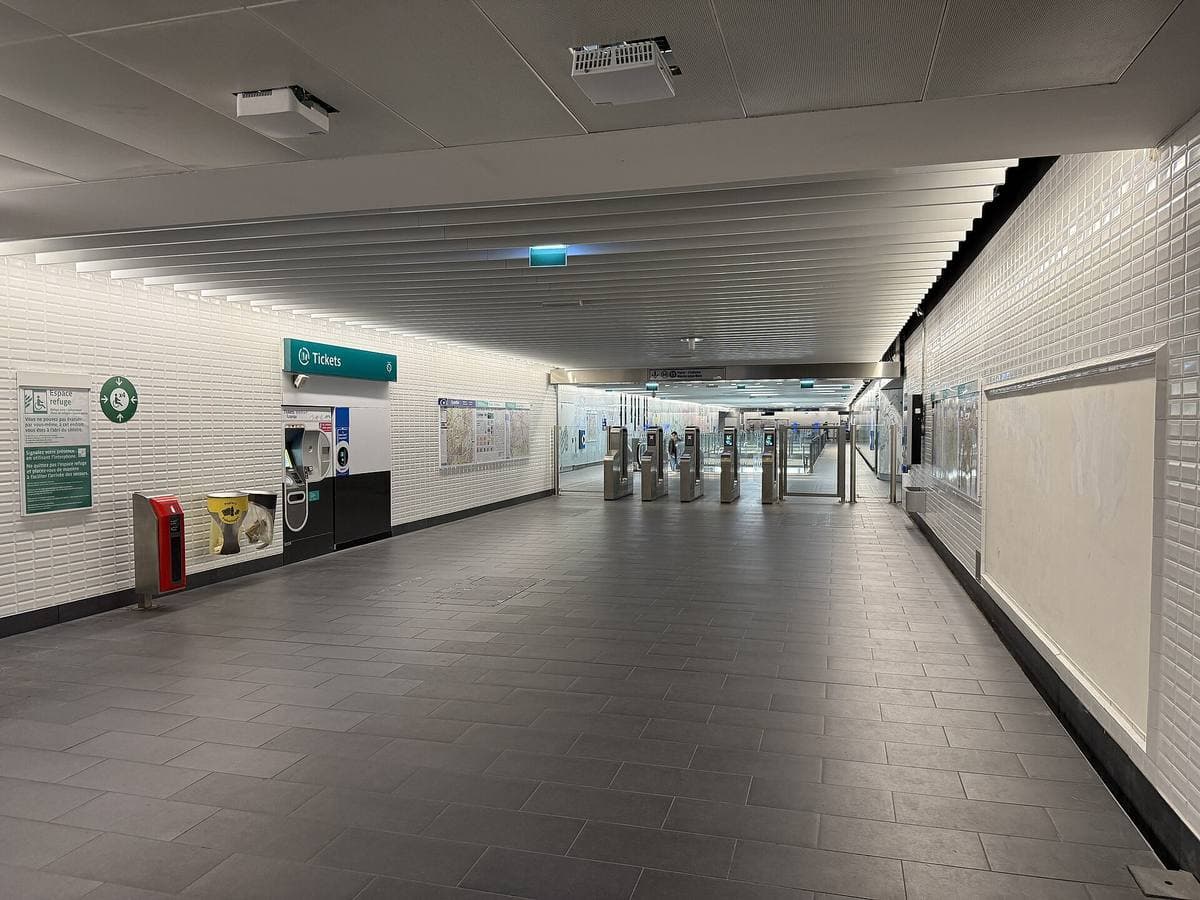 A white metro corridor with ticket barriers at the far end