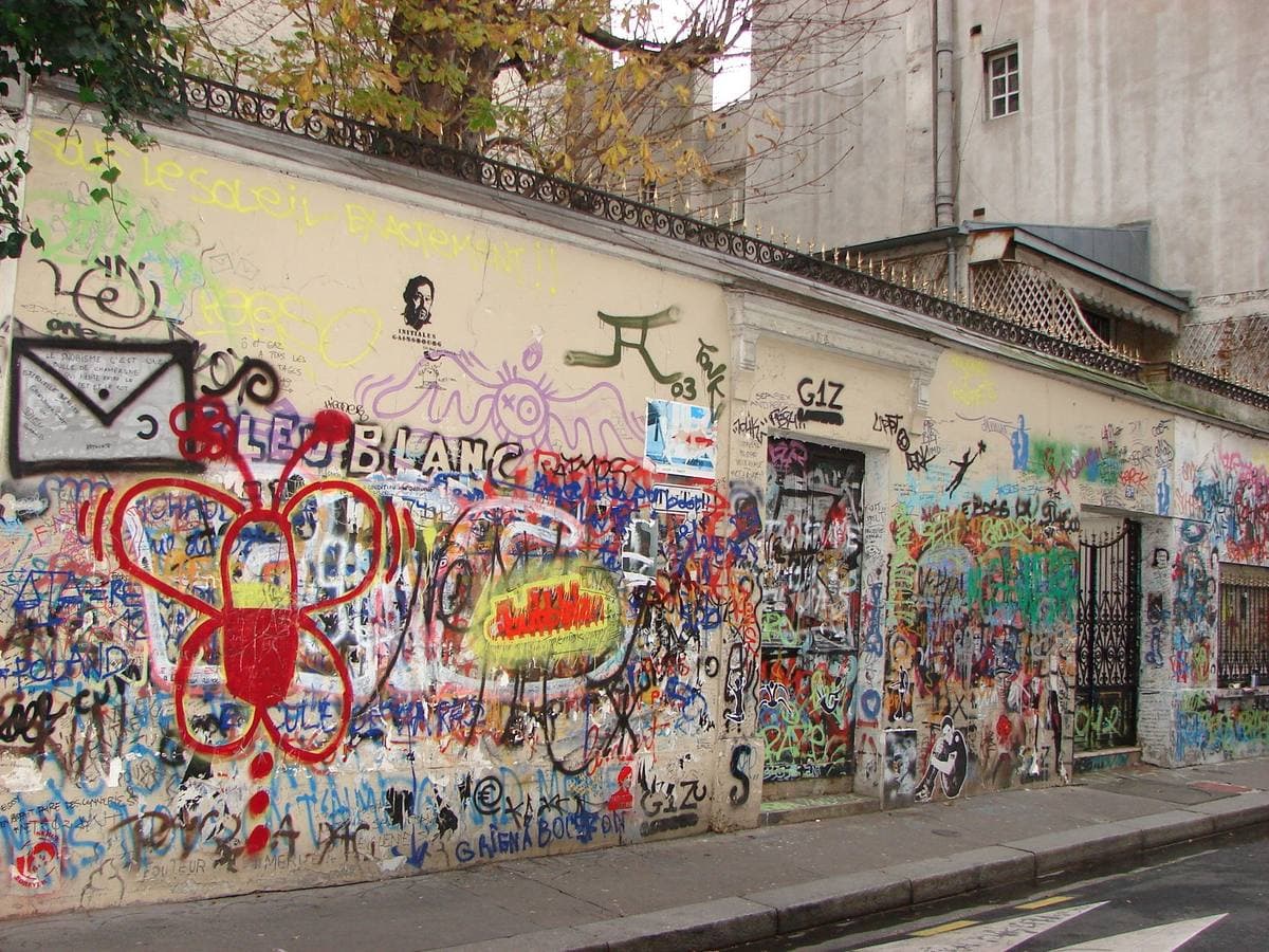 A low white wall covered in hand-written tags, a red flower painted on it