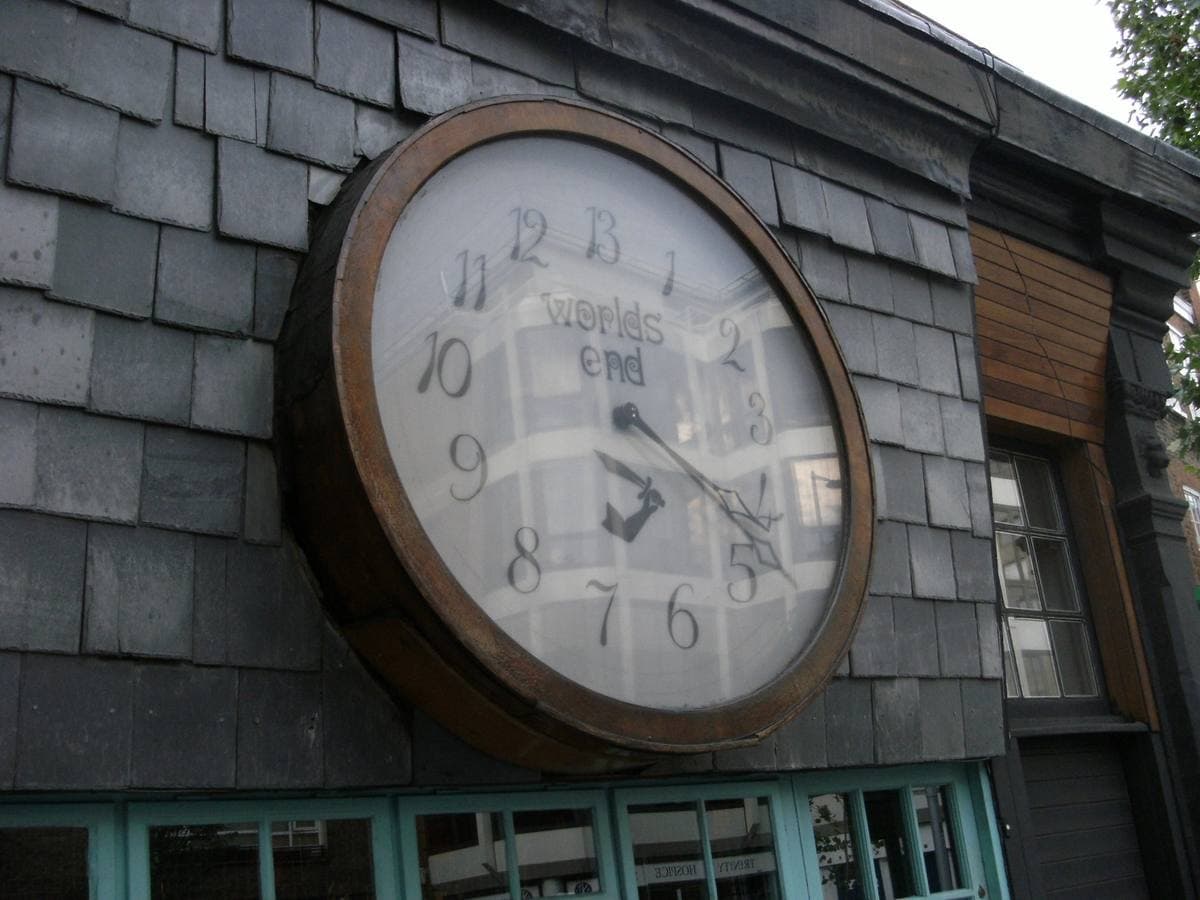 A large clock with thirteen numbers on a slate-hung shop front