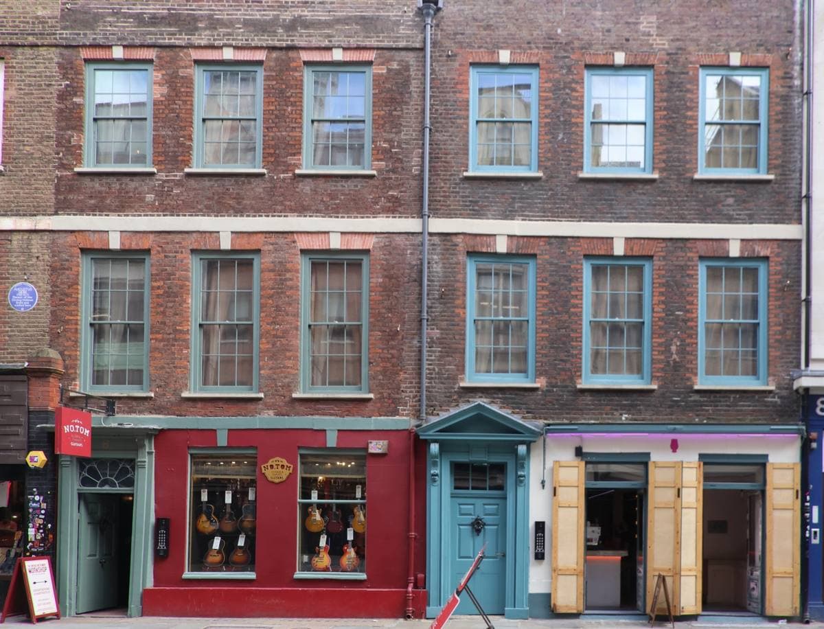 Two narrow brick houses with red and teal shop fronts on Denmark Street