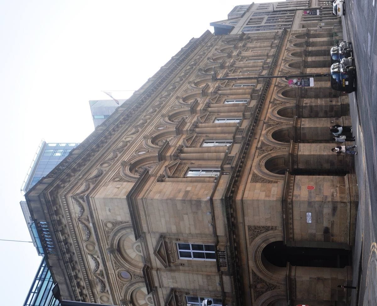 A tall stone palazzo-style hall with arched windows on a Manchester street