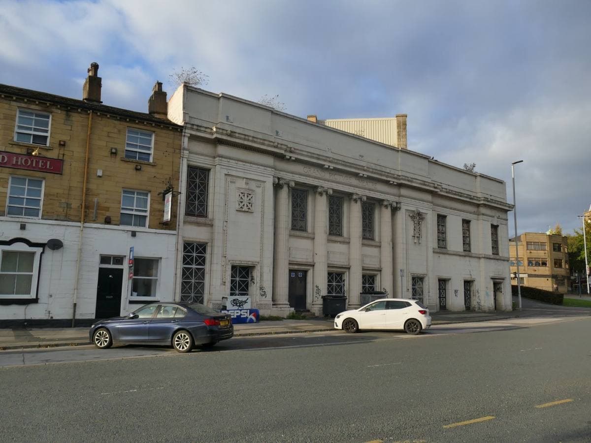 A white classical cinema front beside a small stone terrace on a quiet road