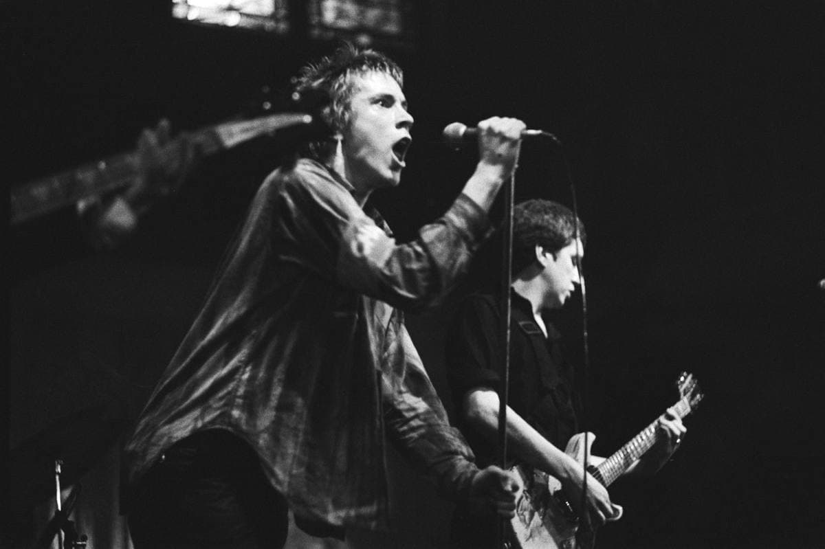 Johnny Rotten leaning into the microphone with Steve Jones on guitar behind him