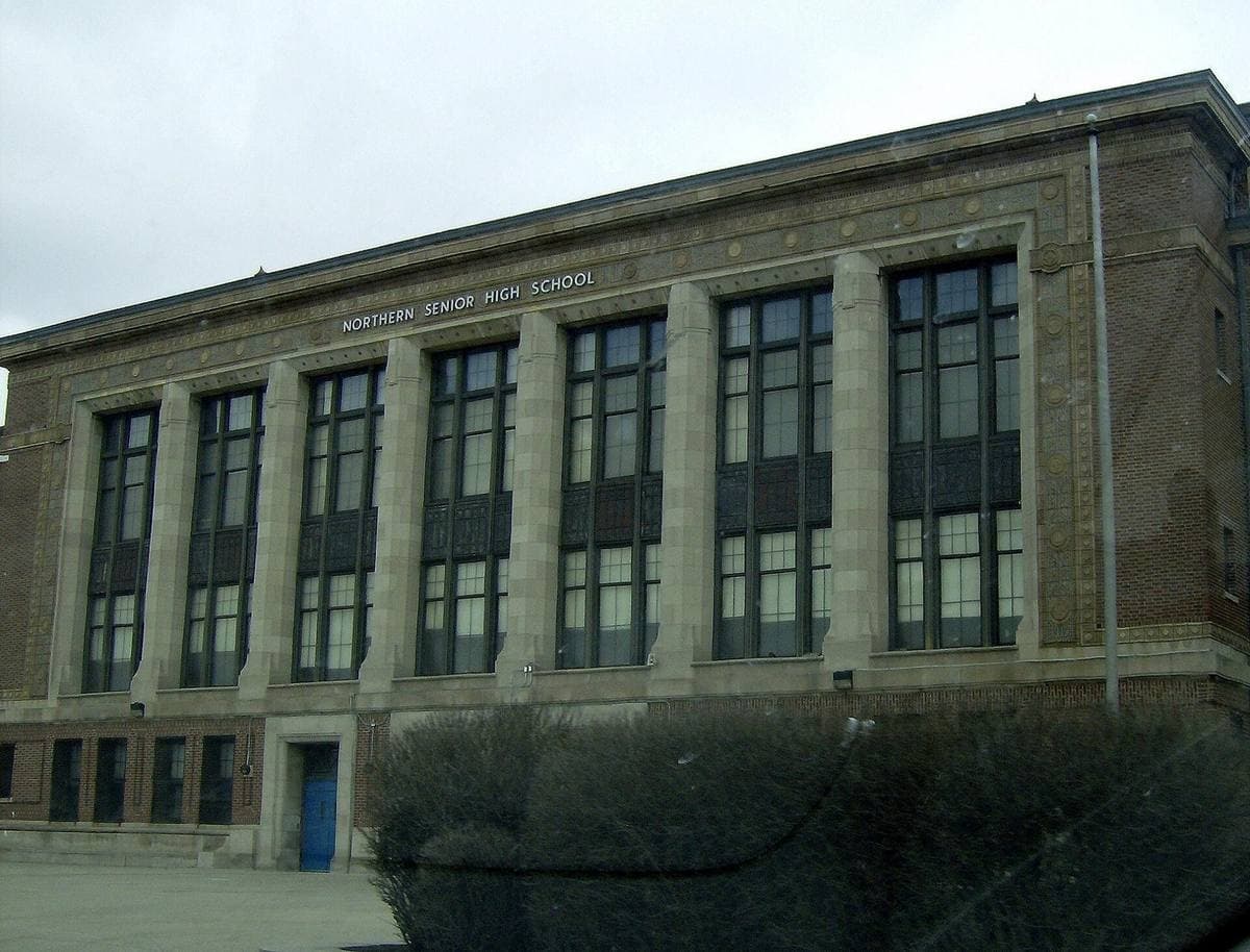 A long brick school building with tall windows behind a lawn