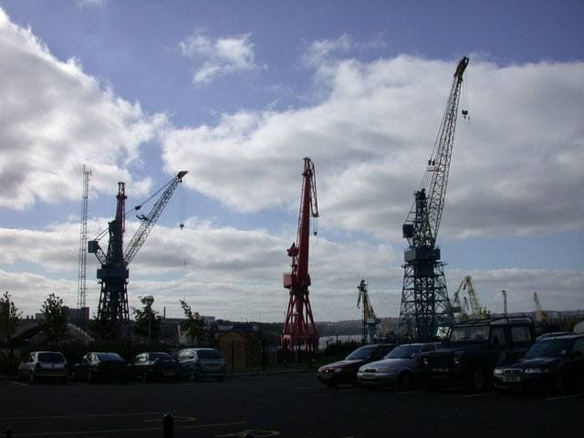 Tall shipyard cranes against the sky above low buildings
