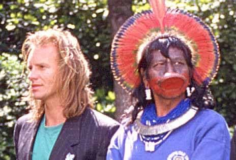 Raoni, wearing a lip plate and feather headdress, beside Sting in a dark jacket