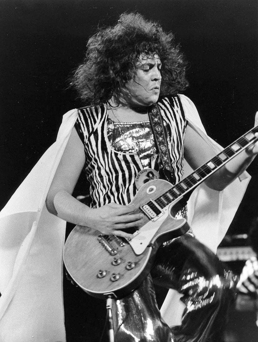 Marc Bolan playing a Les Paul guitar on stage, curls and a striped top