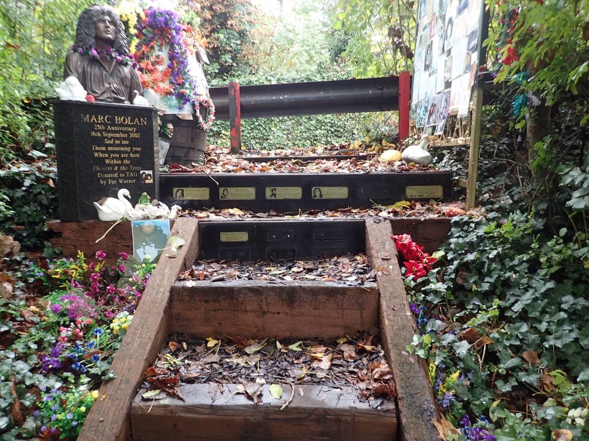 Wooden steps through ivy and flowers up to a bronze bust and a memorial stone