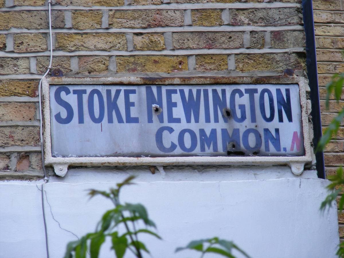 An old enamel street sign reading Stoke Newington Common on a brick wall