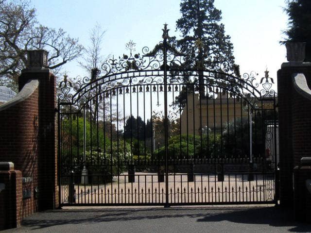 Tall black iron gates between brick piers, trees beyond