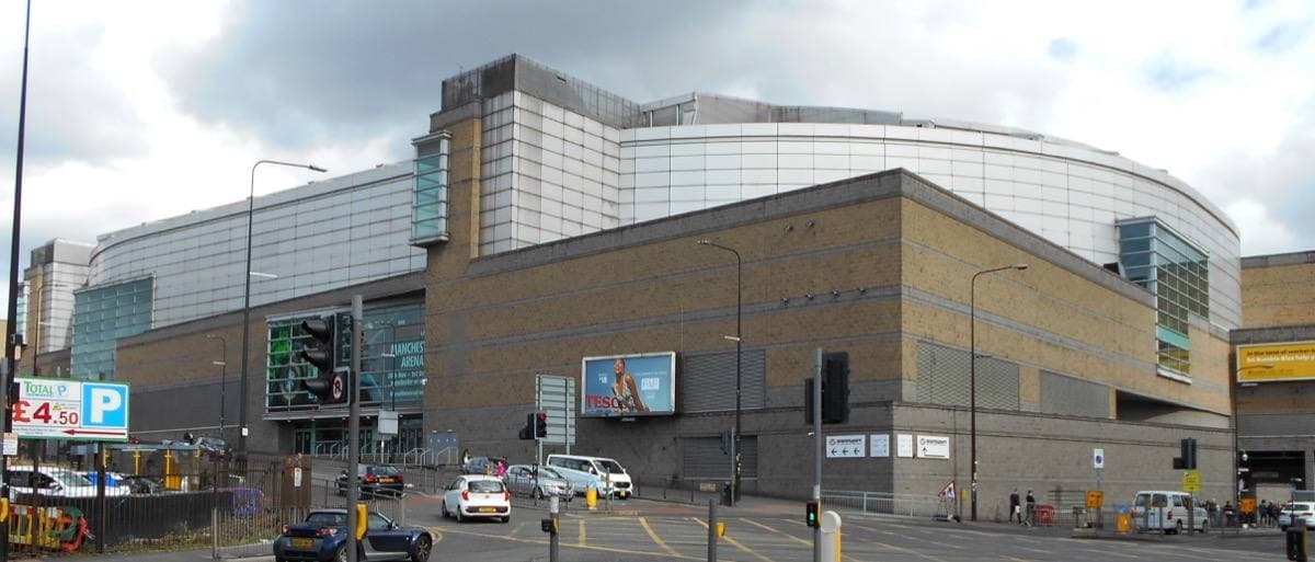 A large brick and glass arena building at a city crossroads