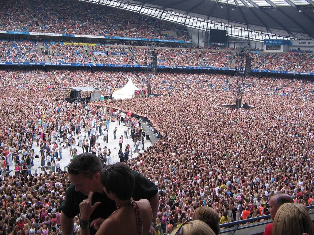 A packed stadium pitch and stands in daylight before a show