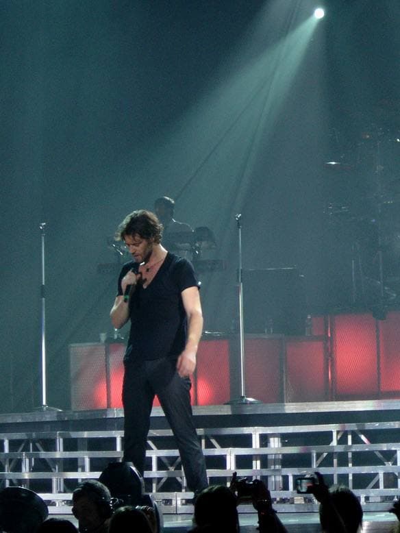 Howard Donald singing in a dark T-shirt under a spotlight