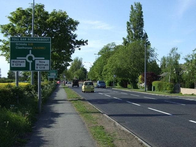 A tree-lined main road with a sign for Toll Bar Roundabout and Waltham