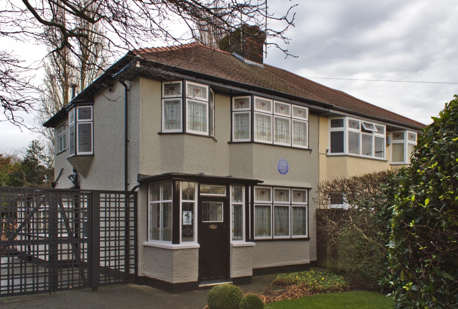 A 1930s semi-detached house with a bay window behind a hedge