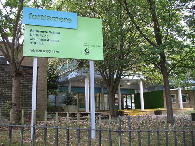 A school sign reading Fortismere in front of low school buildings behind railings