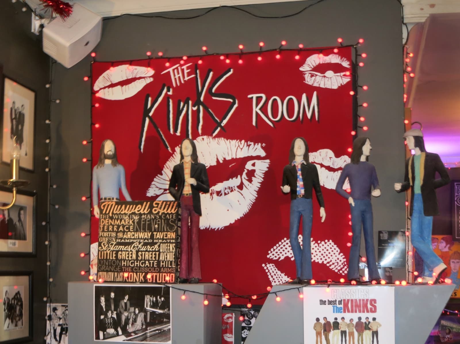 A red sign reading The Kinks Room above figures and framed photographs in a pub