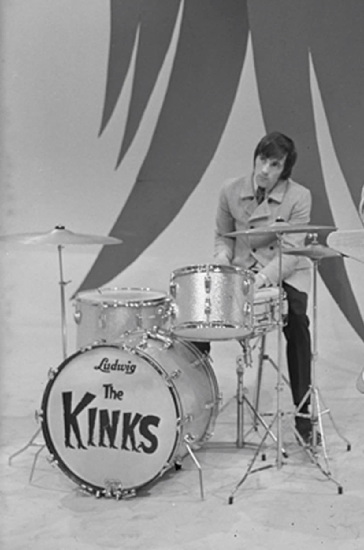 Mick Avory behind a drum kit with The Kinks on the bass drum, in a television studio