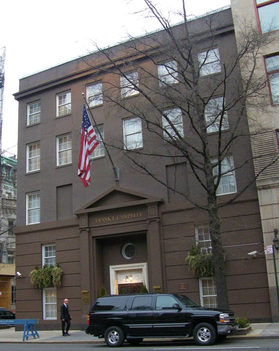 A tall stone building on a Manhattan corner with an American flag over the door