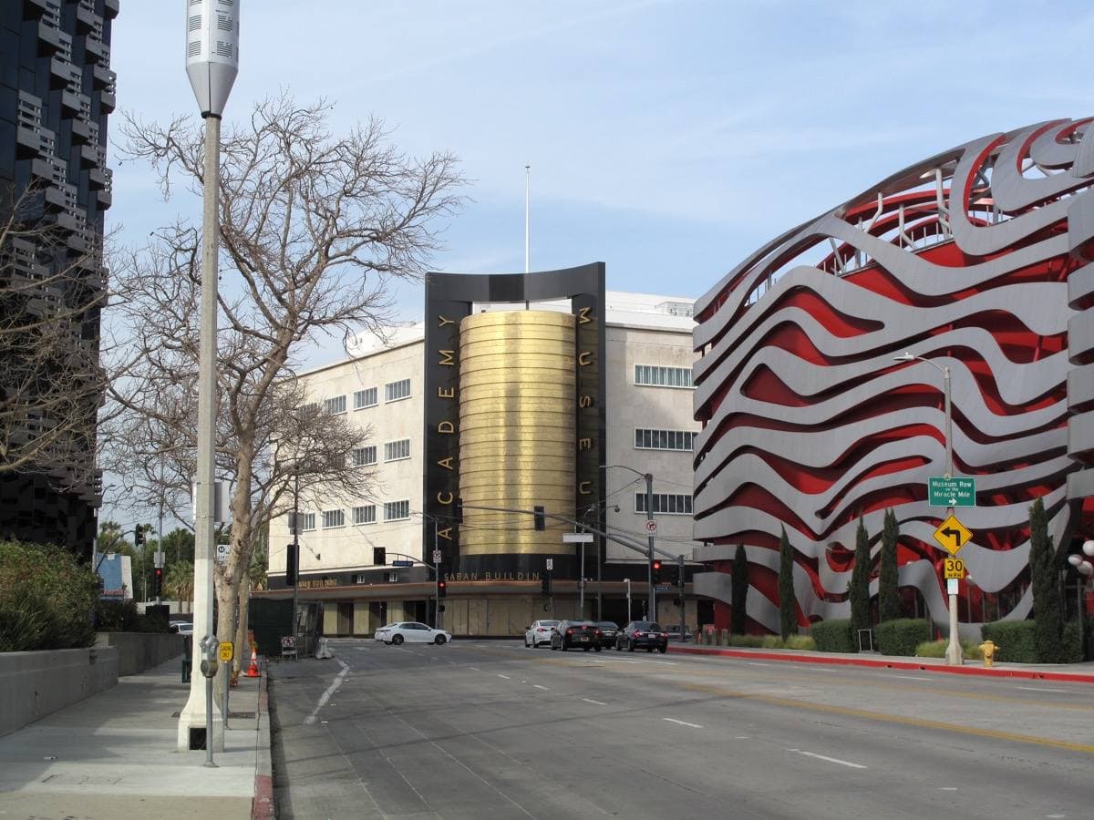 A wide Los Angeles intersection with a gold cylinder building and the ribboned museum