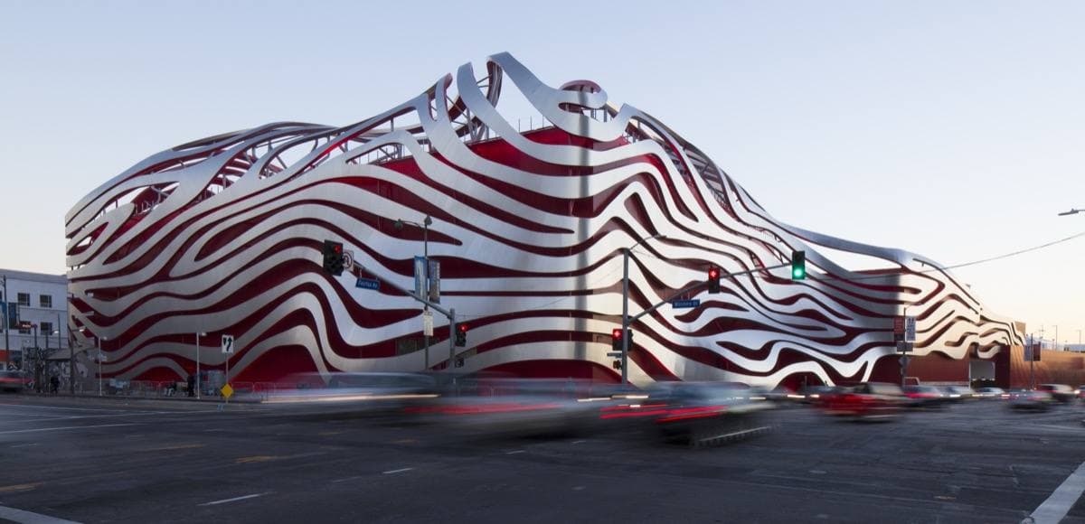 A building wrapped in curving red and silver steel ribbons beside a busy road