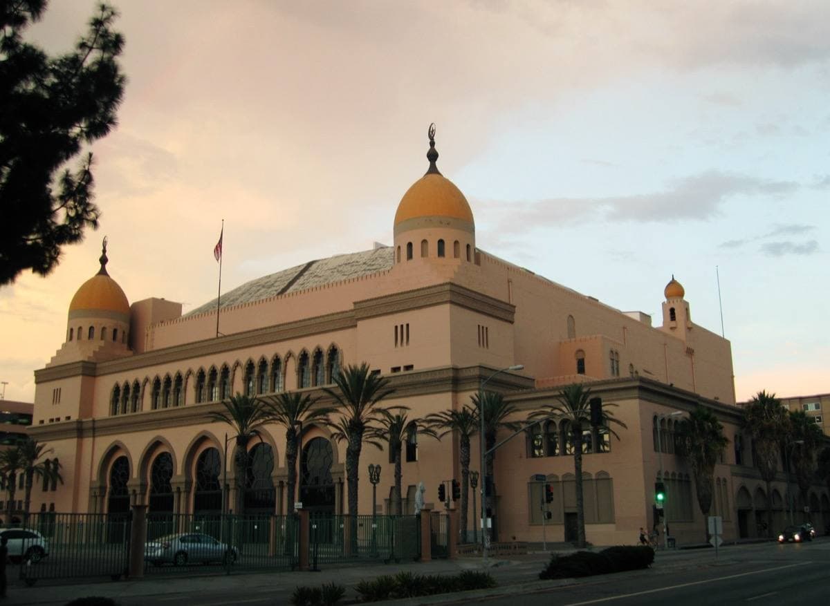A long Moorish-style auditorium with gold domes and palm trees at sunset